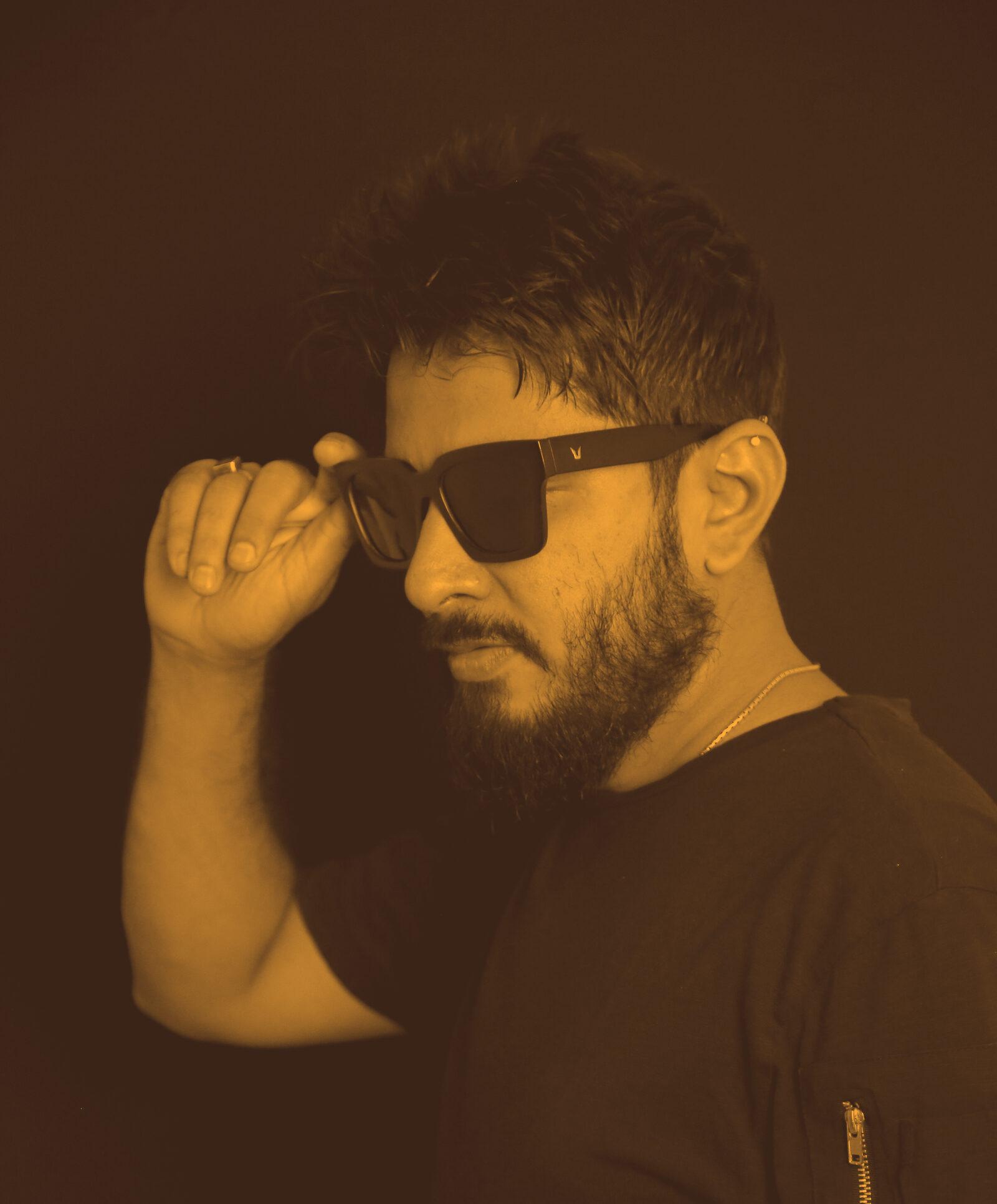Abhi Maisekar in sunglasses, hand at the frames, against a black background.
