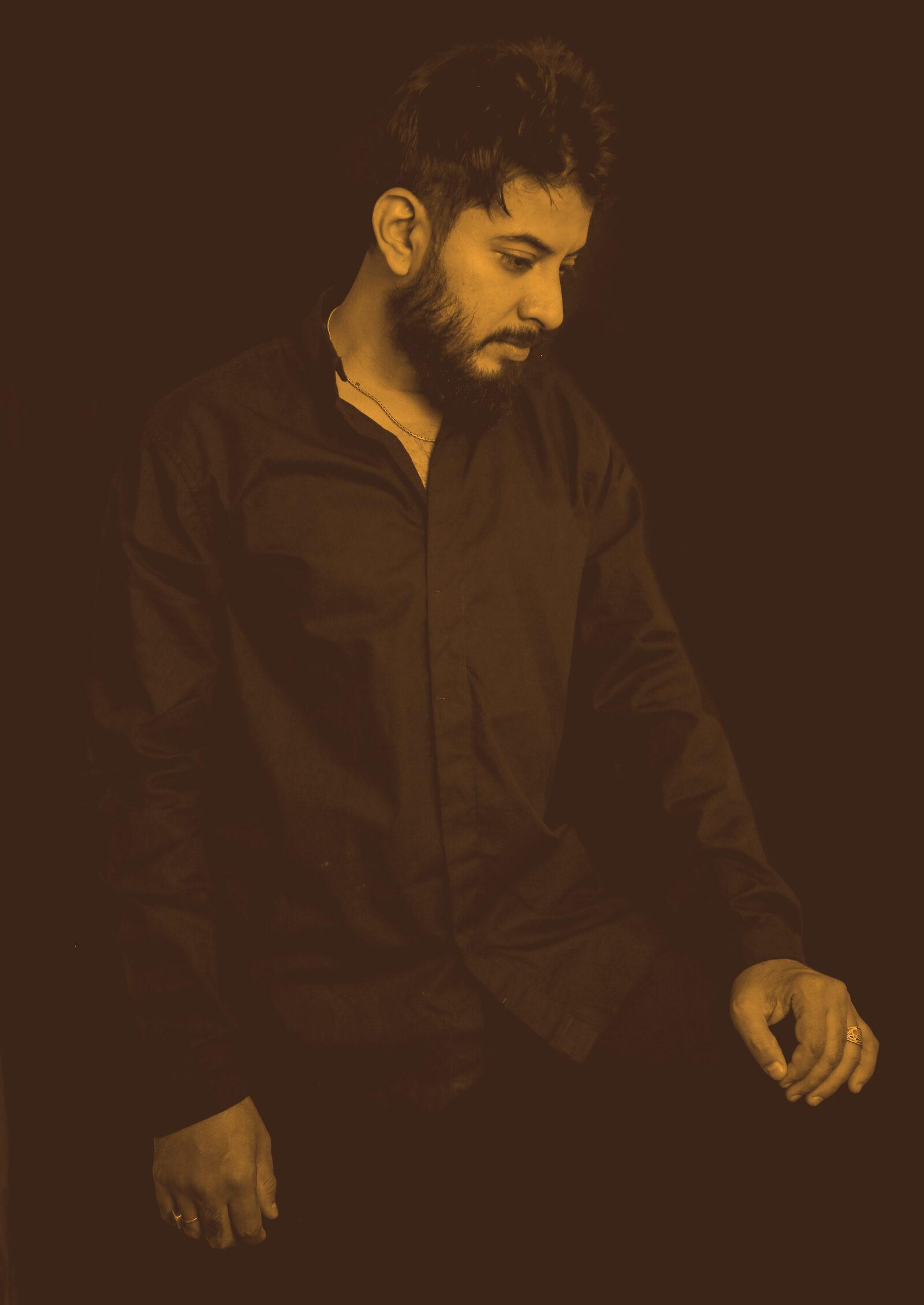 Abhi Maisekar standing with his eyes down, against a black background.