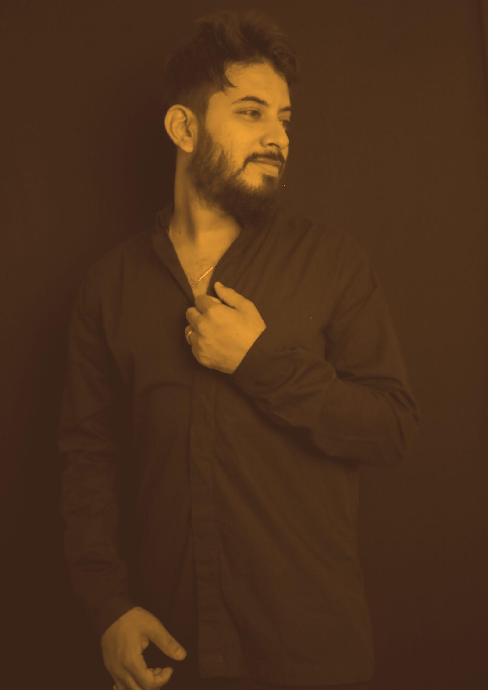 Abhi Maisekar looking off to the side, hand at his collar, against a black background.